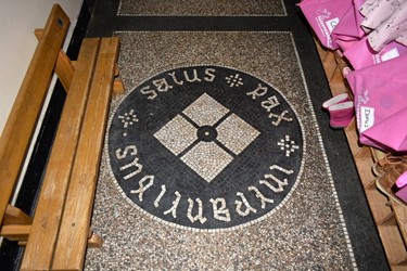 <p>Het ronde motief in de terrazzo vloer met het Latijnse randschift: Salus pax intrantibus (rede en veiligheid voor de binnentredenden).</p>
